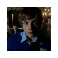 a young man in a blue shirt and tie looking at the camera with other people behind him