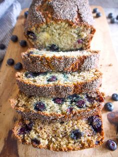 a loaf of blueberry bread on top of a wooden cutting board with fresh blueberries