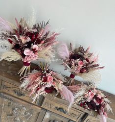 three bouquets of dried flowers and feathers on a dresser