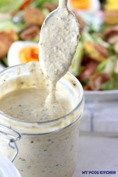 a spoon full of dressing being held up over a bowl with salad in the background