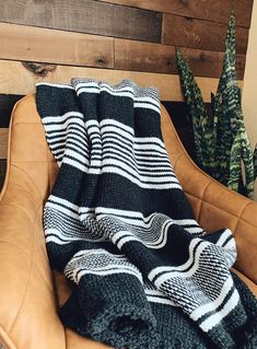 a black and white blanket sitting on top of a leather chair next to a potted plant