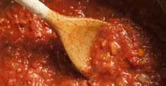 a wooden spoon in a pot filled with red sauce