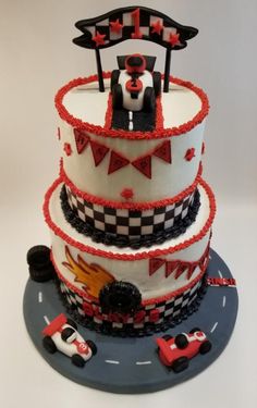 a three tiered cake decorated with cars and bunting on the top is red, white, and black