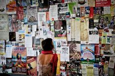 a woman is standing in front of a wall covered with posters and papers that are all over the place