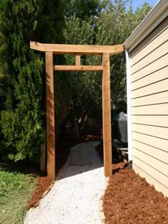 a wooden arbor in the middle of a yard with mulch and dirt around it