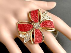 A bright red holiday bow accented with swaths of red glitter and shimmering rhinestone accents has been set upon a gold plated adjustable ring base in this Christmas themed ring that is made to be adjustable from size 6 and up. Bow Size: 50mm x 38mm The gold plated base for this handmade ring is adjustable, which makes this delicate Christmas ring comfortable no matter the size of the wearer's fingers (size 6 and up)  as well as ideal for switching from finger to finger depending on mood or pref Glitter Ring, Christmas Ring, Glam Christmas, Holiday Bows, Bold Rings, Bow Ring, Holiday Gift Wrap, Rhinestone Ring, Red Glitter