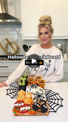 a woman sitting at a kitchen counter with halloween snacks in front of her and the words halloween snack board on it