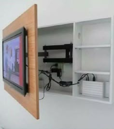 a tv mounted to the side of a white wall next to a shelf with wires