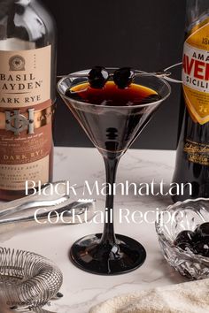 a martini glass filled with black olives next to two bottles of booze