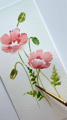 a watercolor painting of pink flowers with green leaves on white paper next to a brush