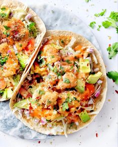 two tacos with shrimp, lettuce and tomatoes on them sitting on a plate