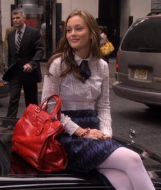 a woman sitting on the back of a car with a red purse in her hand