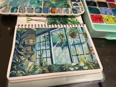 an artist's notebook with watercolors and paintbrushes sitting on a table