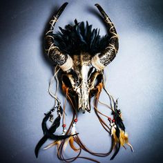 an animal skull with horns and feathers on it's head is displayed against a gray background