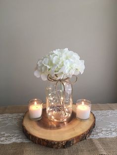 there is a vase with flowers and candles on the wooden table next to two lit candles