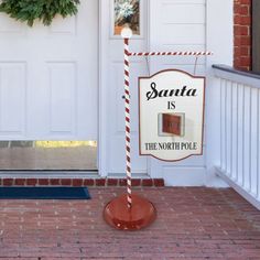 a santa is the north pole sign in front of a door with a wreath on it