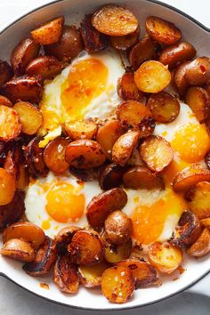 fried eggs and potatoes in a skillet on a white counter top with a spoon