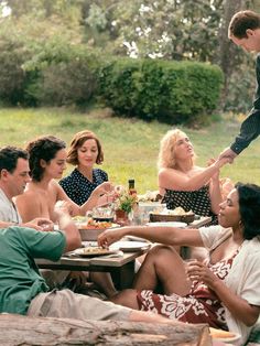 a group of people sitting around a picnic table with food and drinks in front of them