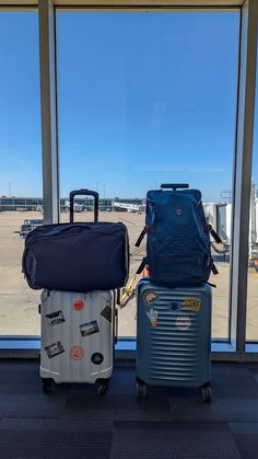 two pieces of luggage sitting next to each other in front of a window with an airport view