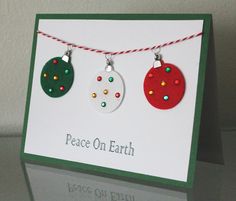 two christmas baubles hanging from a string on a card with the words peace on earth