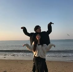 a man and woman standing on the beach with their arms around each other while holding an animal