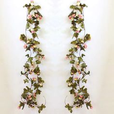 an arrangement of pink flowers and green leaves on a white wall hanging from the ceiling