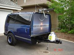 the back end of a blue van parked in front of a house with an antenna attached to it