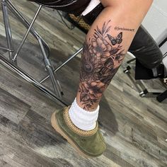 a woman's legs with flowers and butterflies tattooed on her leg, while sitting in a chair