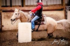 a woman riding on the back of a white horse next to a barrel in an arena