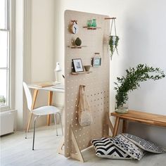 a room with a table, chair and wall mounted pegboard on the wall next to a potted plant