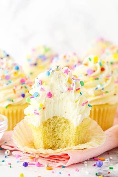 two cupcakes with white frosting and sprinkles on a pink napkin