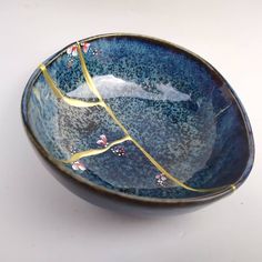 a blue bowl with gold lines and flowers on the rim is sitting on a white surface