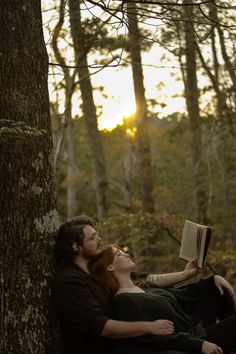 a man and woman laying on the ground next to a tree