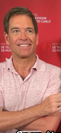 a man with his arms crossed standing in front of a red background