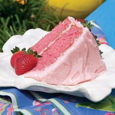 a slice of strawberry cake on a plate with strawberries in the foreground and flowers in the background