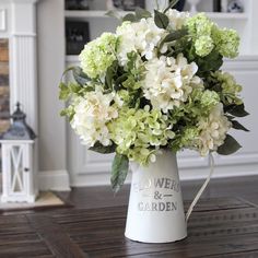 a white vase filled with green and white flowers on top of a wooden table next to a fireplace