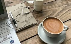 a cup of coffee sitting on top of a wooden table next to a laptop computer