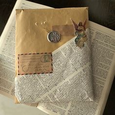 an envelope with two angel charms on it sitting on top of some old book pages