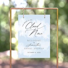 a welcome sign hanging from a gold frame on top of a wooden stand in front of trees