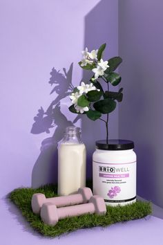 a bottle of milk, two pink dumbs and a flower in a vase