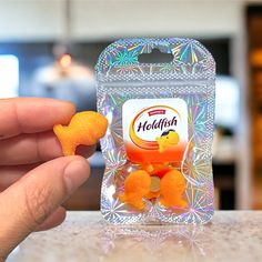 a hand holding a small orange toy in front of a plastic package on a counter