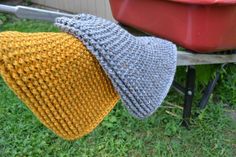 two knitted hats sitting on top of a wooden bench next to a red wheelbarrow