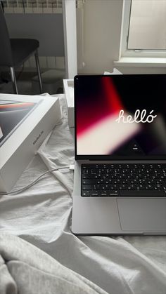 an open laptop computer sitting on top of a bed next to a box and window