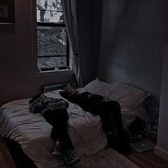 a person laying on top of a bed in a dark room next to a window