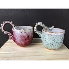 two small cups sitting on top of a wooden table next to each other with handles