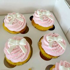 cupcakes with pink frosting and white bows on them in a cardboard box