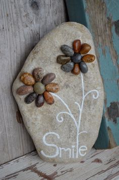 a rock with flowers painted on it and the word smile written in cursive writing