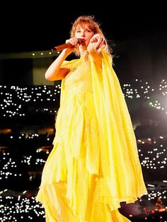 a woman in a yellow dress holding a microphone and singing into the air at a concert