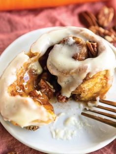 a cinnamon roll with icing and pecans on a white plate next to a fork