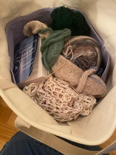 a bag filled with yarn and knitting supplies sitting on top of a wooden floor next to a person